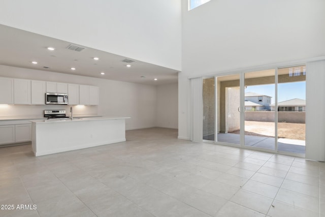 kitchen featuring appliances with stainless steel finishes, a towering ceiling, sink, white cabinets, and a center island with sink