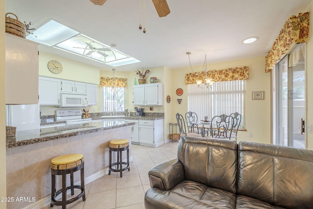 kitchen with white appliances, a breakfast bar area, light tile patterned floors, a skylight, and ceiling fan with notable chandelier