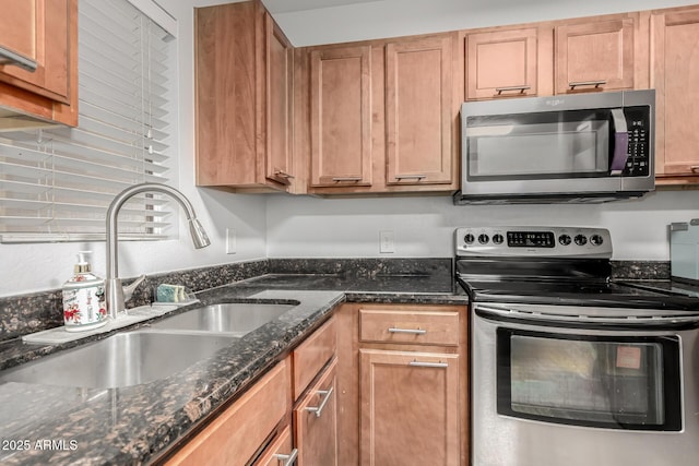 kitchen featuring appliances with stainless steel finishes, dark stone counters, and sink