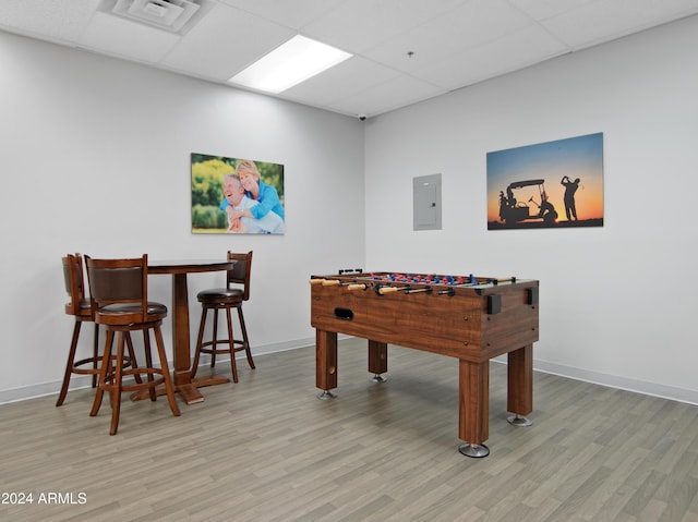 recreation room featuring a drop ceiling, electric panel, and light hardwood / wood-style flooring