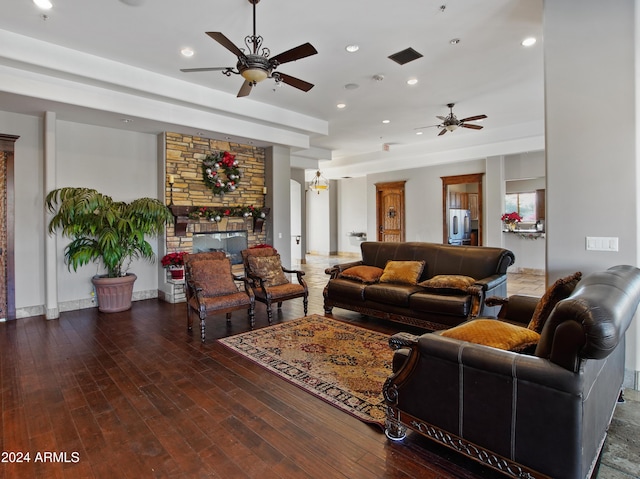 living room featuring dark hardwood / wood-style flooring, ceiling fan, and a stone fireplace