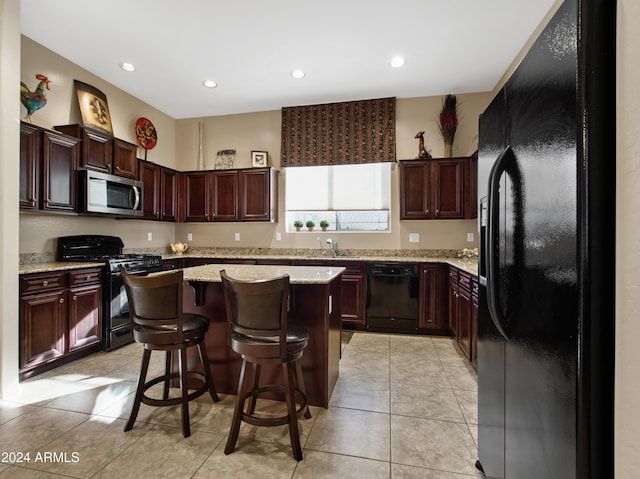 kitchen featuring a breakfast bar area, light stone countertops, black appliances, a center island, and sink