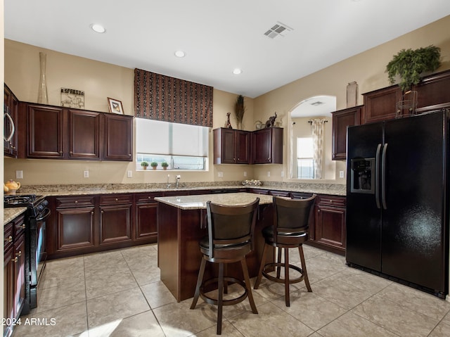 kitchen featuring light stone counters, black appliances, light tile patterned flooring, a center island, and a kitchen bar