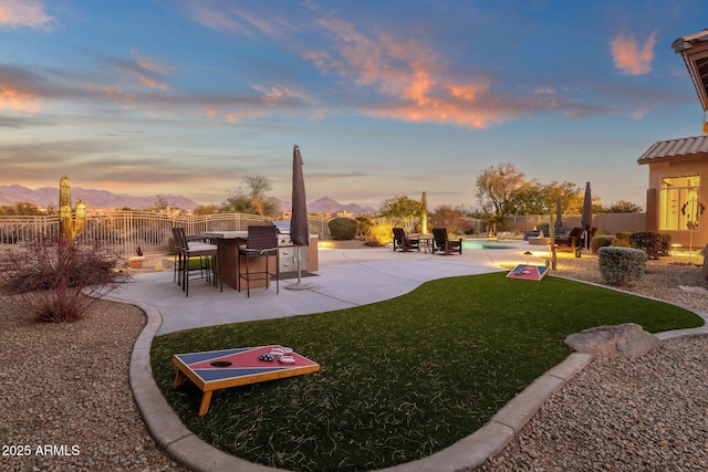 yard at dusk featuring a fenced in pool, a patio, exterior bar, a mountain view, and exterior kitchen