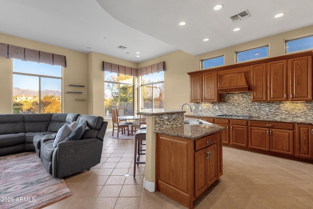 kitchen with premium range hood, sink, a breakfast bar area, an island with sink, and stone counters