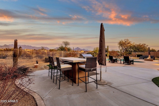 patio terrace at dusk featuring a bar, a mountain view, and area for grilling