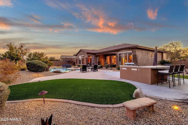 back house at dusk with a patio, a yard, and an outdoor bar