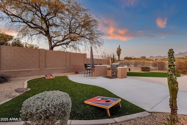 yard at dusk featuring an outdoor kitchen and a patio