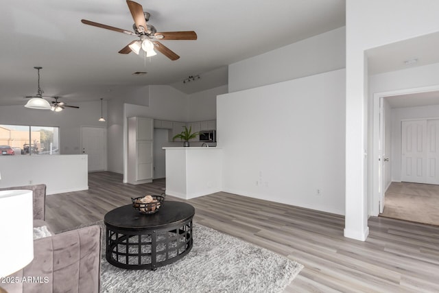 living room with ceiling fan, light hardwood / wood-style flooring, and vaulted ceiling