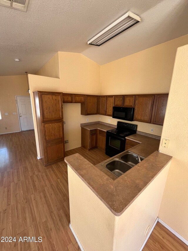 kitchen featuring lofted ceiling, black appliances, sink, a textured ceiling, and kitchen peninsula