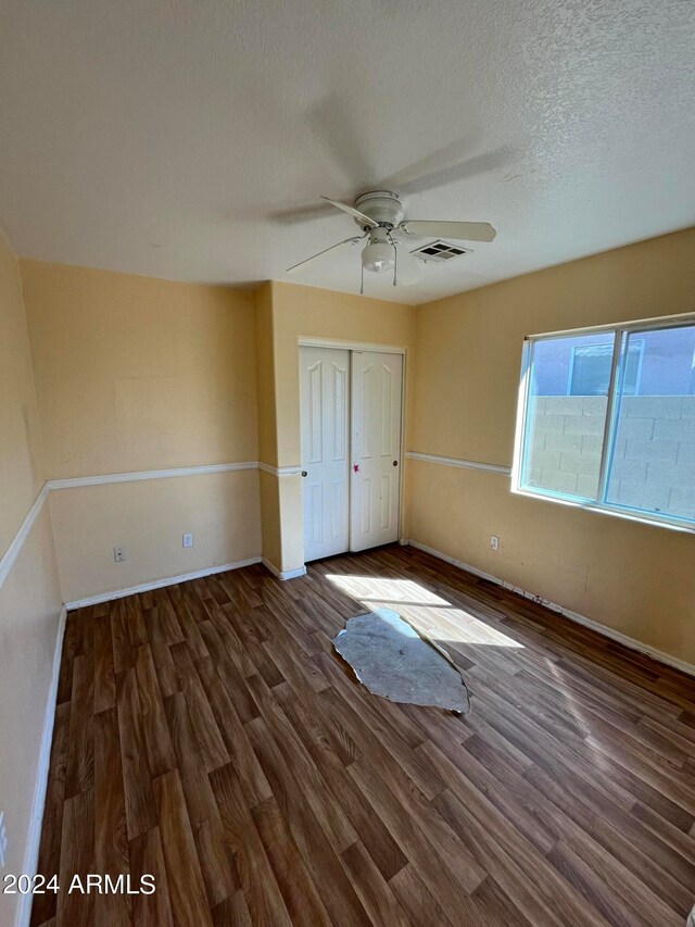 unfurnished bedroom featuring a textured ceiling, a closet, ceiling fan, and dark wood-type flooring