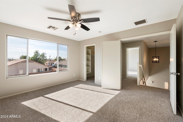 unfurnished bedroom featuring a walk in closet, a closet, carpet, and ceiling fan with notable chandelier