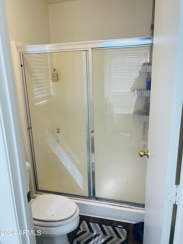 bathroom featuring hardwood / wood-style floors, toilet, and a shower with shower door