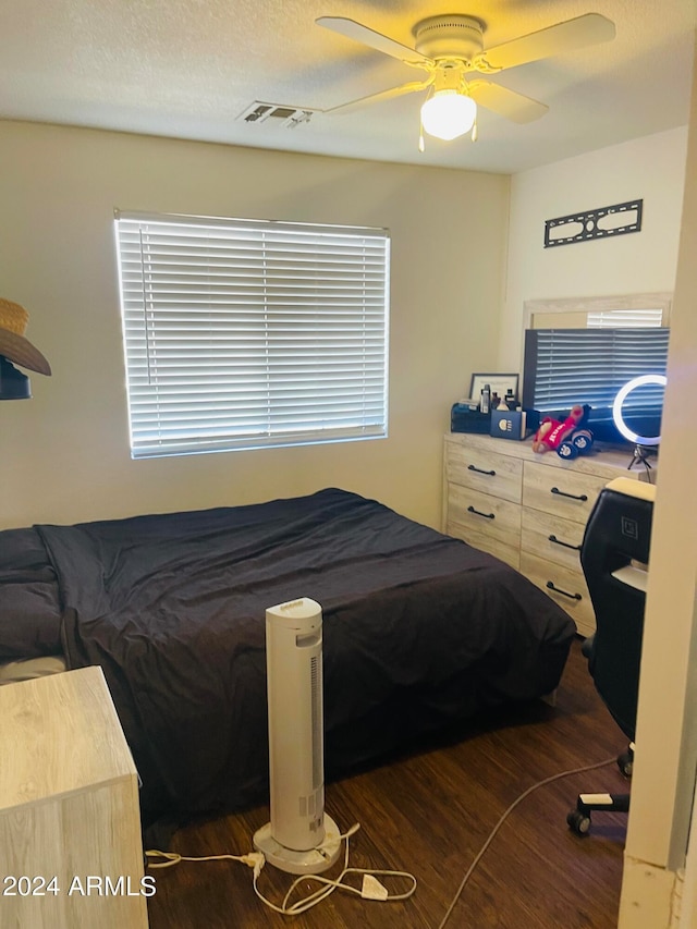 bedroom with a textured ceiling, dark wood-type flooring, and ceiling fan