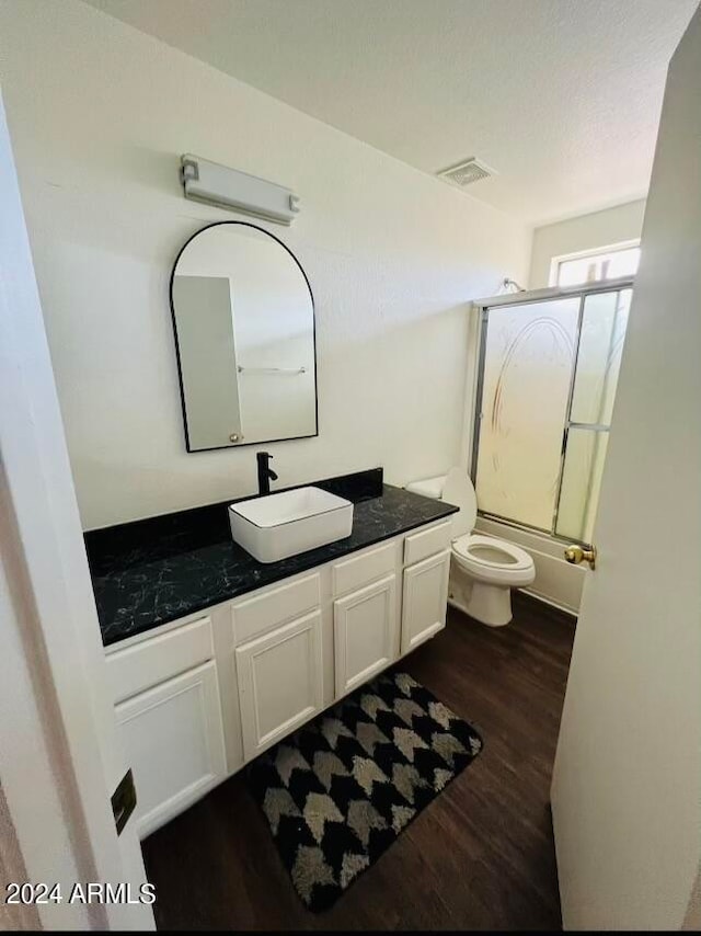 full bathroom featuring wood-type flooring, toilet, vanity, and combined bath / shower with glass door