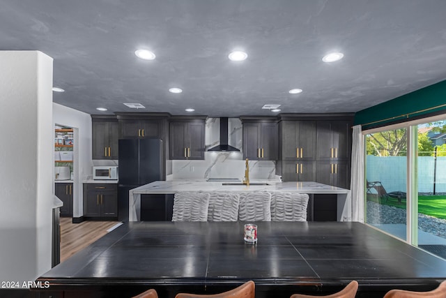 kitchen featuring a center island, sink, wall chimney exhaust hood, black refrigerator, and light wood-type flooring