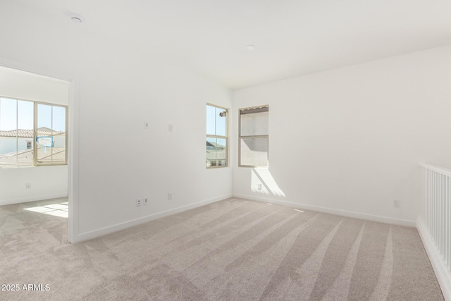 spare room with a healthy amount of sunlight, baseboards, and light colored carpet