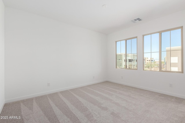 spare room featuring light colored carpet, visible vents, and baseboards