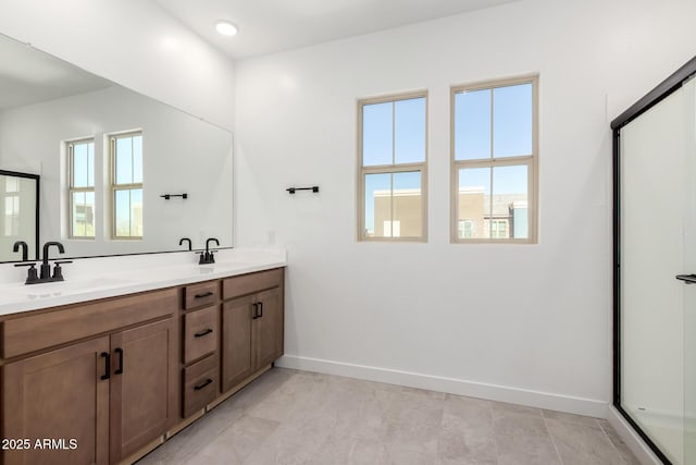 full bath with an enclosed shower, a sink, baseboards, and double vanity