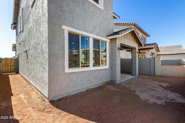 view of home's exterior with a tiled roof, fence, and stucco siding