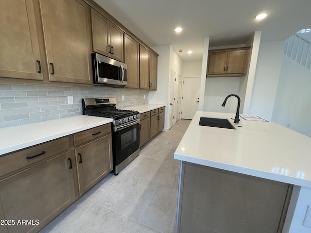 kitchen with appliances with stainless steel finishes, backsplash, a sink, and light countertops