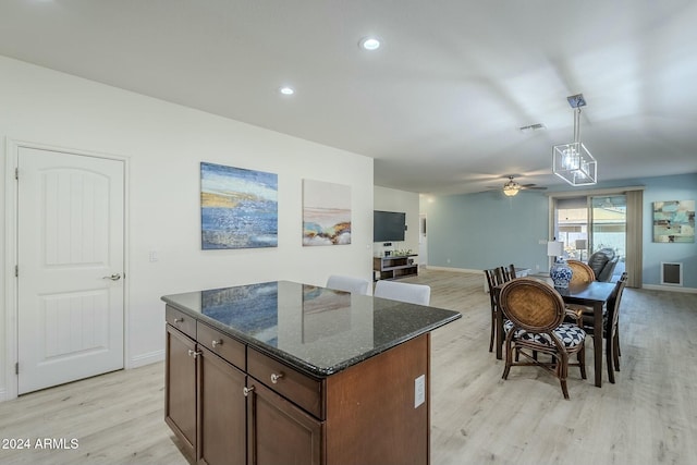 kitchen with dark stone counters, ceiling fan, a center island, light hardwood / wood-style floors, and hanging light fixtures