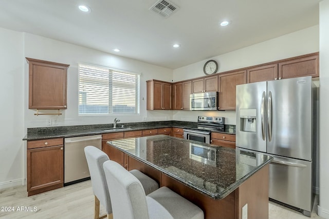 kitchen with sink, dark stone countertops, light hardwood / wood-style floors, a kitchen island, and appliances with stainless steel finishes