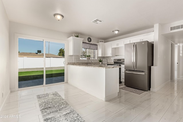 kitchen with light stone countertops, backsplash, kitchen peninsula, white cabinets, and appliances with stainless steel finishes