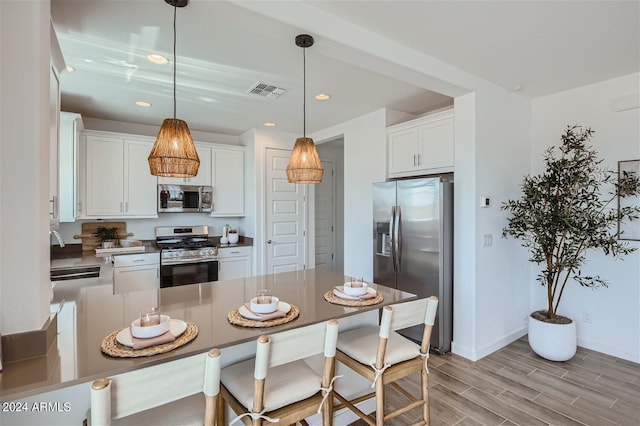 kitchen with sink, white cabinetry, hanging light fixtures, stainless steel appliances, and light hardwood / wood-style floors