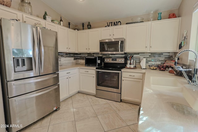 kitchen featuring light tile patterned flooring, vaulted ceiling, decorative backsplash, white cabinets, and appliances with stainless steel finishes