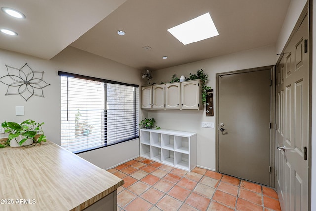 kitchen with light tile patterned floors, a skylight, and white cabinets