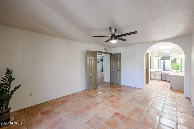 unfurnished bedroom with ensuite bathroom, light tile patterned floors, ceiling fan, and a textured ceiling