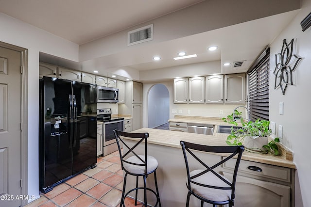 kitchen with stainless steel appliances, light tile patterned flooring, a breakfast bar area, and kitchen peninsula