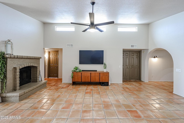 unfurnished living room featuring light tile patterned flooring, a brick fireplace, a textured ceiling, and ceiling fan