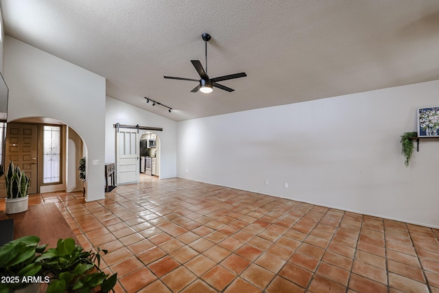 unfurnished living room with vaulted ceiling, light tile patterned floors, ceiling fan, a barn door, and a textured ceiling