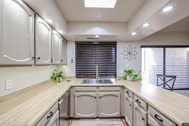 kitchen with a skylight, dishwasher, sink, and kitchen peninsula