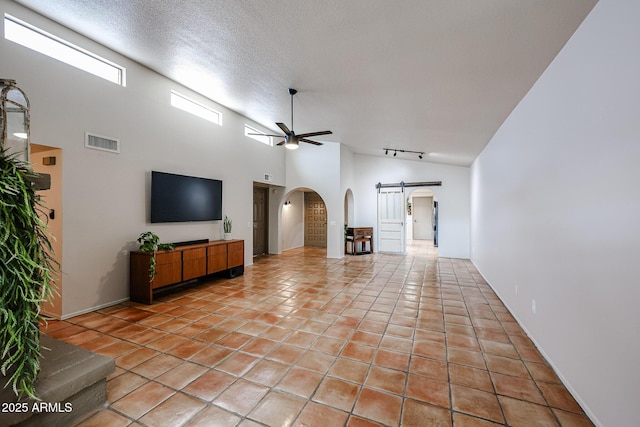 tiled living room with rail lighting, high vaulted ceiling, a textured ceiling, ceiling fan, and a barn door