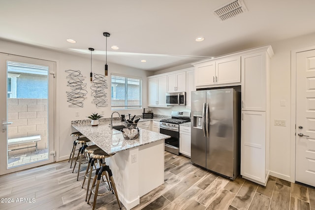 kitchen with appliances with stainless steel finishes, light stone counters, light hardwood / wood-style flooring, white cabinetry, and hanging light fixtures