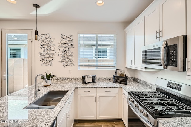 kitchen with light stone countertops, sink, hanging light fixtures, stainless steel appliances, and white cabinets