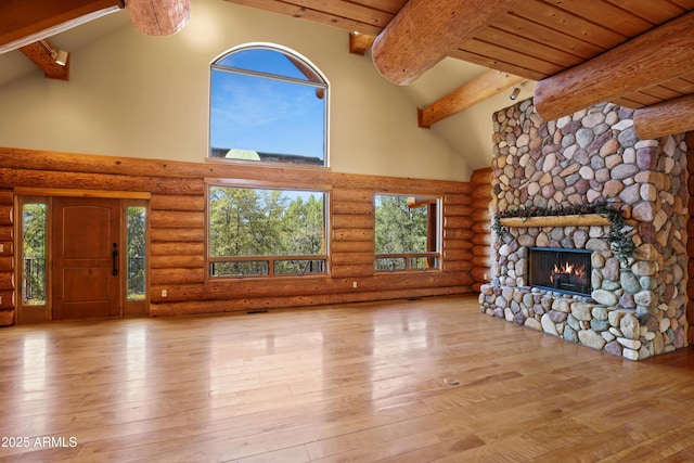 unfurnished living room featuring a stone fireplace, rustic walls, high vaulted ceiling, beamed ceiling, and hardwood / wood-style floors