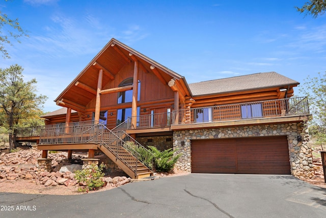 cabin with driveway, log siding, a garage, stairs, and stone siding