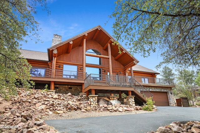 view of front of home with stone siding, driveway, log exterior, stairway, and a chimney