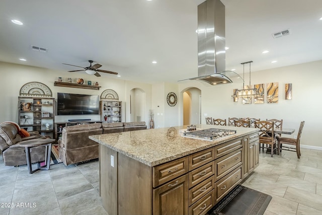 kitchen with stainless steel gas cooktop, light stone counters, island range hood, decorative light fixtures, and a center island