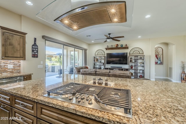 kitchen featuring stainless steel gas stovetop, light stone countertops, ceiling fan, and decorative backsplash