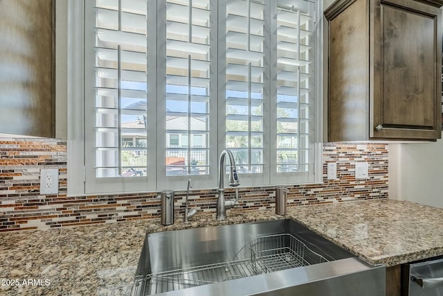 kitchen with light stone countertops, sink, backsplash, and dark brown cabinets