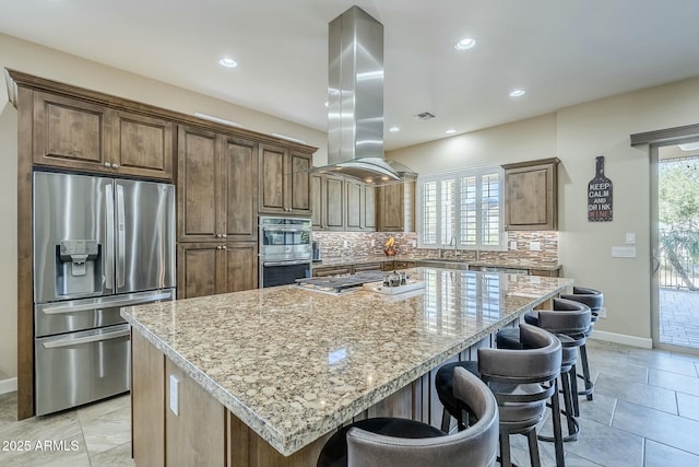 kitchen featuring light stone counters, island range hood, stainless steel appliances, and a kitchen island