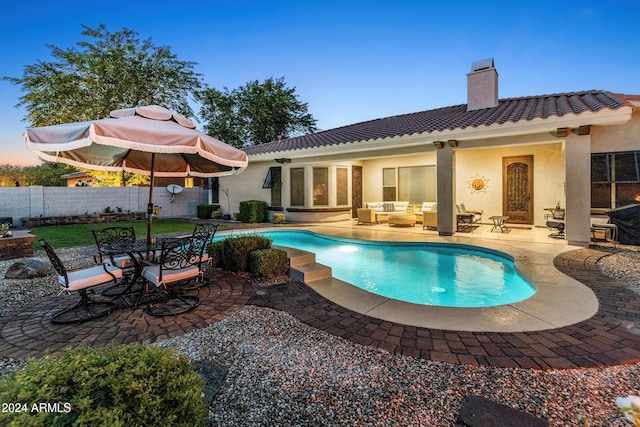 pool at dusk with outdoor lounge area and a patio