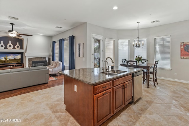 kitchen with sink, stainless steel dishwasher, dark stone countertops, an island with sink, and pendant lighting