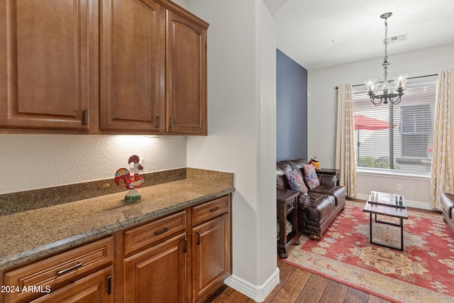 kitchen with hardwood / wood-style floors, pendant lighting, light stone counters, and a notable chandelier