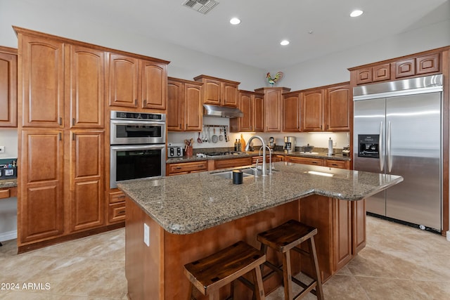 kitchen featuring sink, a kitchen breakfast bar, stone countertops, a kitchen island with sink, and appliances with stainless steel finishes